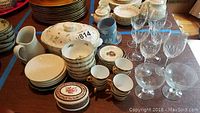 Full lot overview showing mixed serving pieces including Wedgewood cups and saucers, small plates, bowls, glass stemware and other porcelain items on wood table