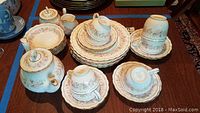 Full set showing cups stacked on saucers with plates, bowls, teapot, sugar bowl, and creamer arranged on table
