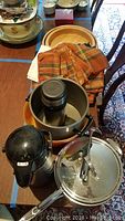 Overview photo showing a variety of kitchen items on a table including pots, pans, bowls, towels, and a coffee thermos.