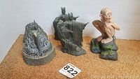 Five figurines set on a flat surface with a tag number 822, showing detailed sculptural elements from Lord of the Rings including Minas Tirith and character figures such as Gollum and Sauron.