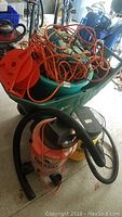 Photo showing two shop vacuums (Ridgid and Genie), green plastic wheelbarrow packed with extension cords.