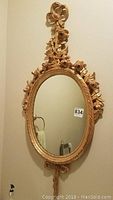 Full view of ornate gold framed oval mirror hung on wall showing entire frame and mirror glass
