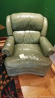 Front view of the green leather recliner chair showing overall worn condition, visible scratches, and cushioned armrests and back.