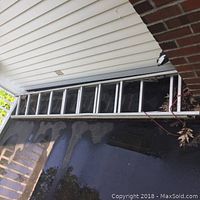 Full side view of the aluminum extension ladder extended and resting on the ground and a porch.
