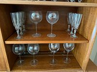 Top shelf showing 4 plain balloon wine glasses centered and 9 cut-crystal goblets at sides