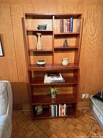 Full view of stacked teak shelving unit against wood panel wall
