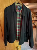 Front view of black jacket on hanger showing plaid lining and logo