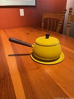 Side view of yellow enamel fondue pot on tray, showing wood handle and lid