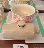 Chamber pot with red floral pattern and stoneware bed warmer displayed together