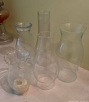 Group of five clear glass chimneys showing varied shapes and candle residue