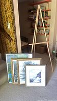 Four framed prints and wooden easel grouped together