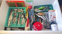 Drawer view showing Empire steak knife box, assorted flatware in green trays, multiple kitchen utensils in baskets