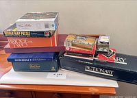 Stack of boxed games, puzzle, and playing cards showing titles on spines