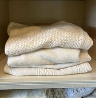 Stack of four cream sweaters showing textures