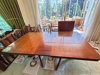 Dining table top with two leaves installed, chairs visible alongside, extra leaf shown upright
