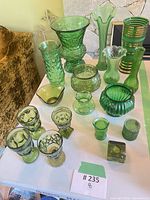 Group shot of green glass vases, bowls, goblets, candle holders on table