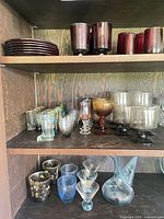 Three shelves showing full assortment of coloured glassware and porron