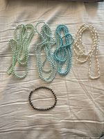 Four pastel tone faux-pearl necklaces laid out with one dark bracelet