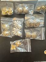 All eight pairs of earrings in individual bags laid out on black surface