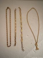 Four gold-plated chains laid out: two necklaces and two bracelets