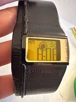 Front view showing amber LCD screen, gold bezel and black leather cuff strap