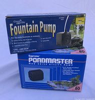 Stacked retail boxes of Green Harvest Fountain Pump Model 80 and Supreme Pondmaster Mag-Drive Utility Pump