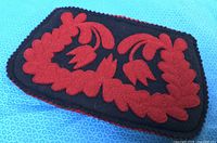 Front view of black wool felt clutch with red floral appliqué and scalloped edging