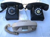 Group shot of three telephones: two black rotary, one beige push-button