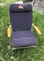 Front view of folding deck chair displaying royal blue fabric, chrome frame, wooden armrests, padded headrest with nautical flag emblem