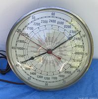 Front view of round electric world time clock with metal rim, glass face, paper dial, two hands, power cord visible