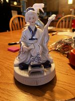 Front view of ceramic geisha figurine holding shamisen on rotating base