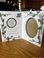 Front view of hinged porcelain frame showing both openings, floral relief and silver 25 emblem