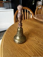 Full view of brass bell with wooden handle on table