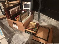 Box of assorted wood and metal picture frames with mats visible