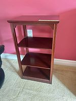 Full view of cherry veneer 3-shelf end table against pink wall