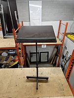 Full view of music stand on platform showing wood top, metal shaft, cross base