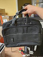 Front view of black canvas laptop bag showing faux leather panel, handles and zipper
