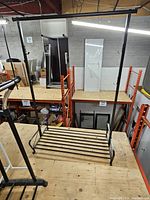 Full view of black metal garment rack on platform showing hanging bar and lower slat shelf