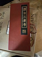 Red presentation box exterior with gold-on-black Chinese title label and ribbon tie