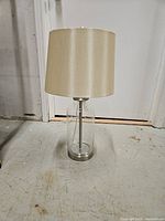 Full view of lamp showing glass base, metal accents, fabric shade
