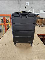 Front view of black hard-shell suitcase showing ridged exterior and spinner wheels
