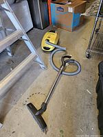 Canister vacuum with hose, wand and brush laid out on floor