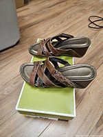 Side view of both sandals on box showing wedge heel, straps and overall style