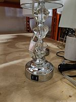Close view of one lamp base showing chrome finish, faceted glass column, clear cord and dual USB ports