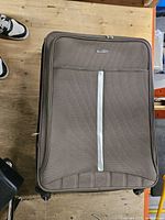 Front view of brown Polo World suitcase showing fabric texture, front pocket, vertical accent, wheels
