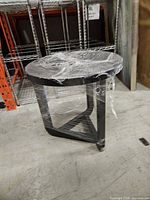 Full view of round dark brown side table wrapped in plastic