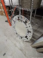 Front view of round silvertone Greek key mirror leaning against shelving