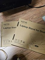 Two boxed Suptek LS001 laptop stands on floor