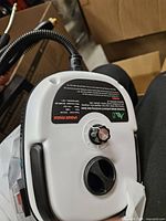 Top view of white/black steam cleaner showing control knob, warning label and hose connection