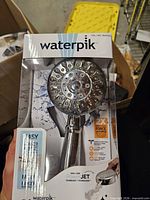 Front of sealed retail box showing Waterpik ShowerClean Pro handheld shower head